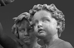 Detailaufnahme einer Skulptur aus Mamor. Es sind zwei gelockte Kinderköpfe zu erkennen.