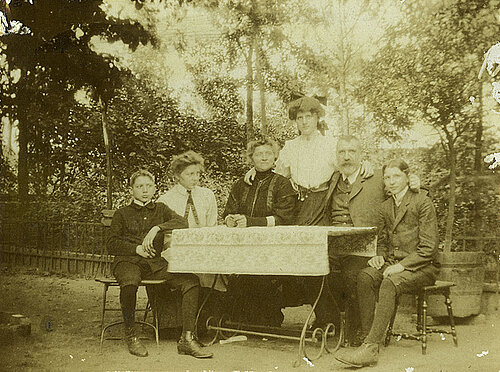 Schwarzweißfoto einer Familie an einem Tisch im Garten. 