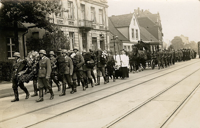 Schwarzweißfoto eines Trauerzuges mit Soldaten, Messdienern und einem Sarg auf einer Trauerkutsche