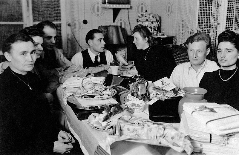 Schwarzweißbild: Eine Familie sitzt um einen Gabentisch, der reich gefüllt ist.