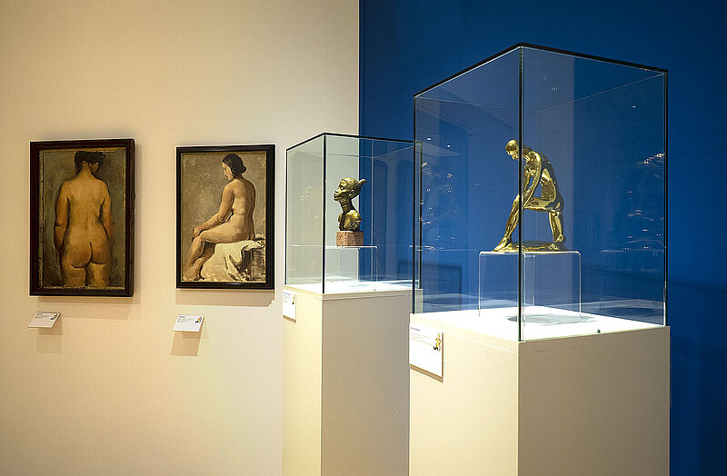 Von links nach rechts: Gemälde einer unbekleideten Frau von hinten, Gemälde einer unbekleideten Frau von der Seite, goldene Büste einer Frau, goldene Skulptur einer unbekleideten Frau.