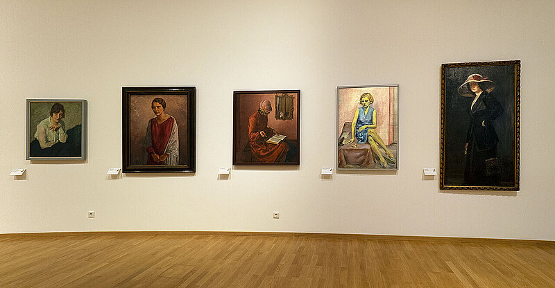 Fünf Gemälde von Frauen in verschiedenen Lebenssituationen an einer Wand.